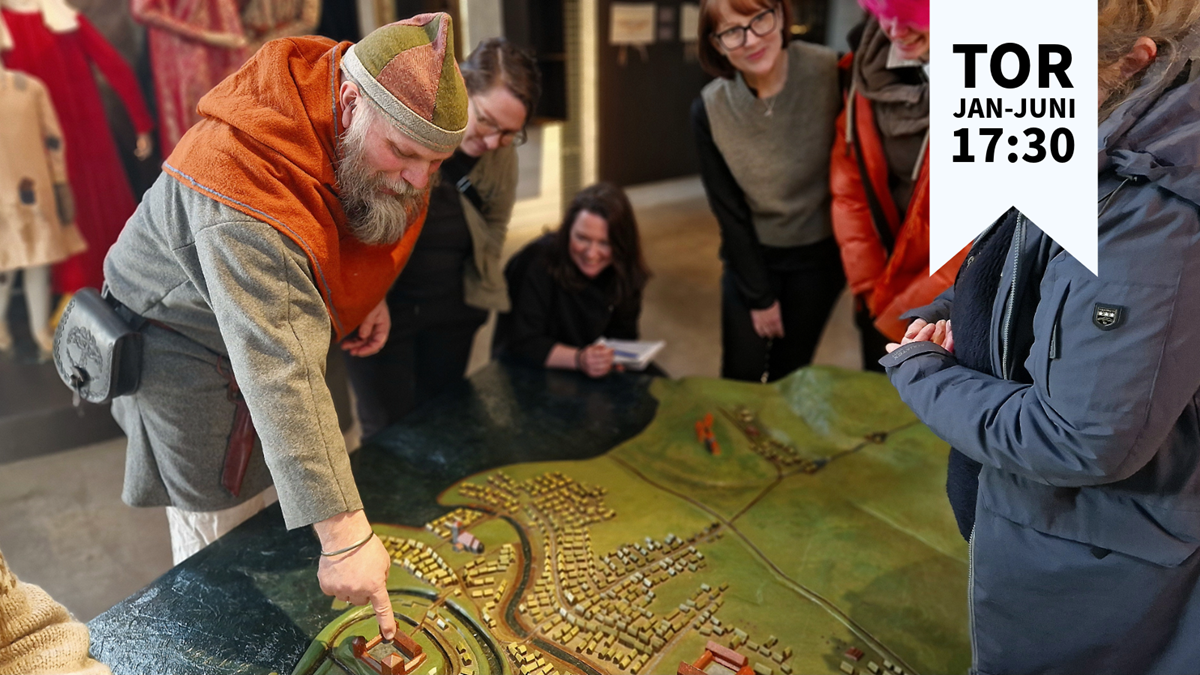 En man i vikingatida kläder pekar på en stadsmodell för publik
