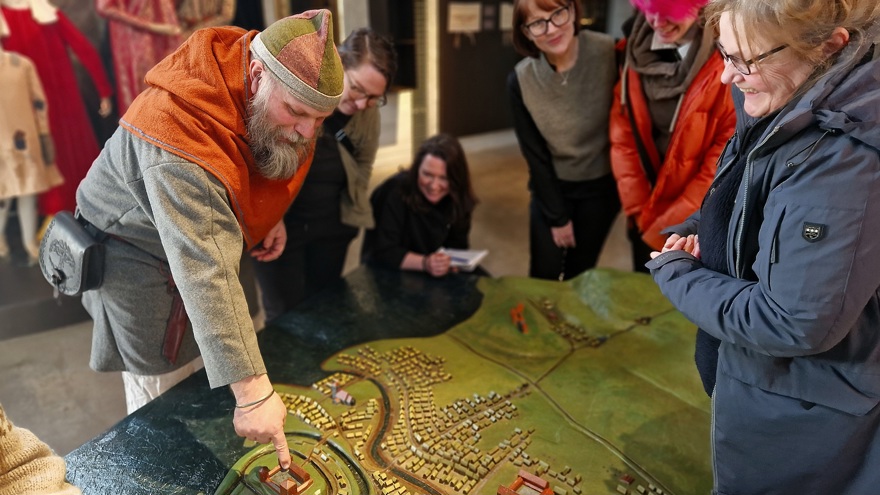 En man i vikingatida kläder pekar på en stadsmodell för publik
