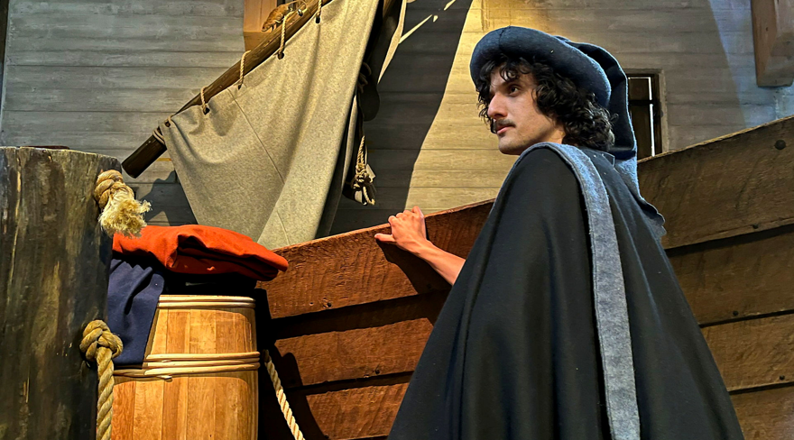 A man portraying Pietro Querini in front of a boat, looking out over the horizon.