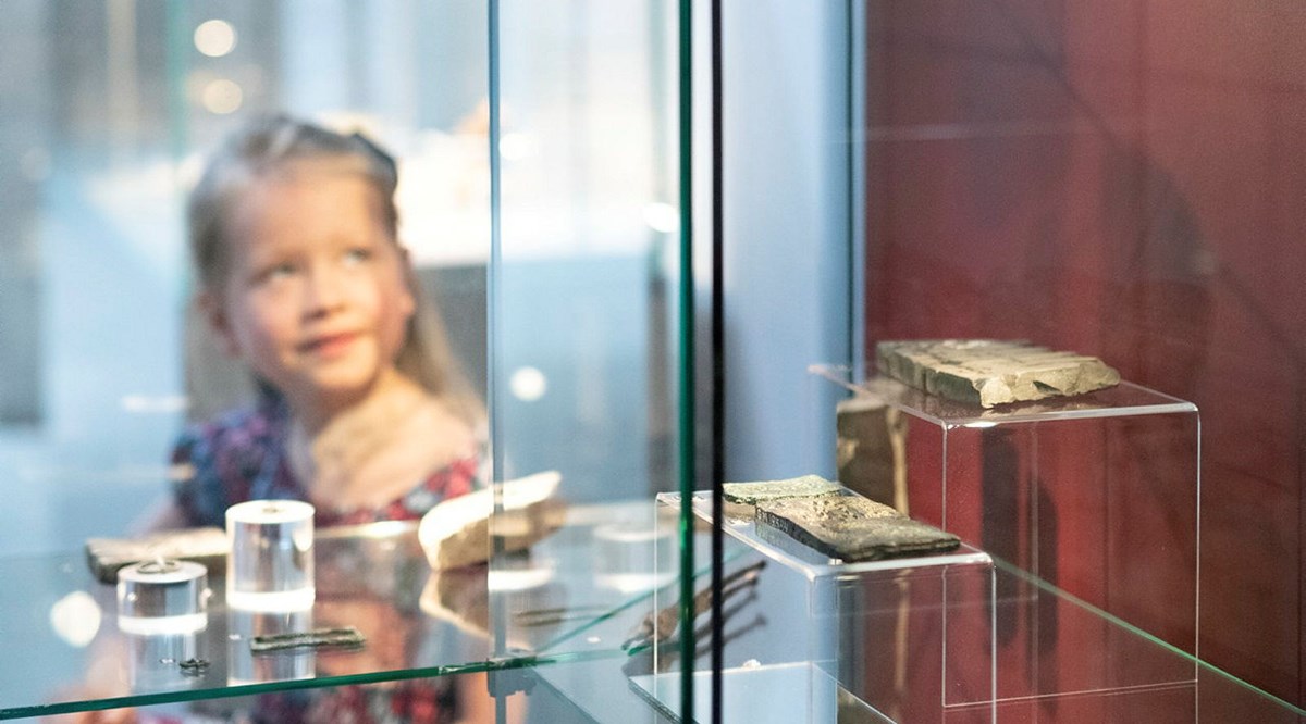 I förgrunden syns en glasmonter med arkeologiska föremål i. I bakgrunden skymtar ett barn.