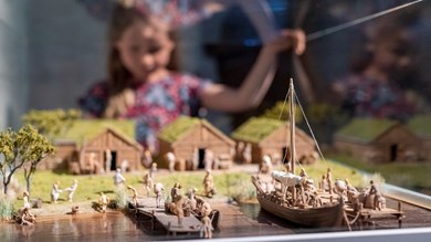 Ett barn skymtas i bakgrunden, i förgrunden modeller av en hamn med båtar och människor