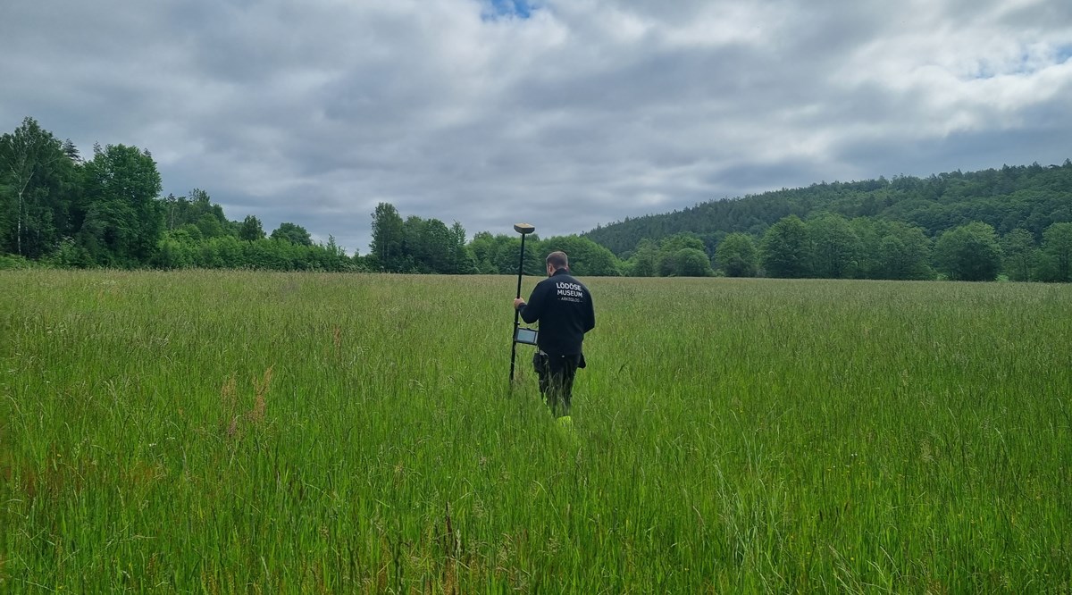 En arkeolog med GPS-utrustning går på ett fält