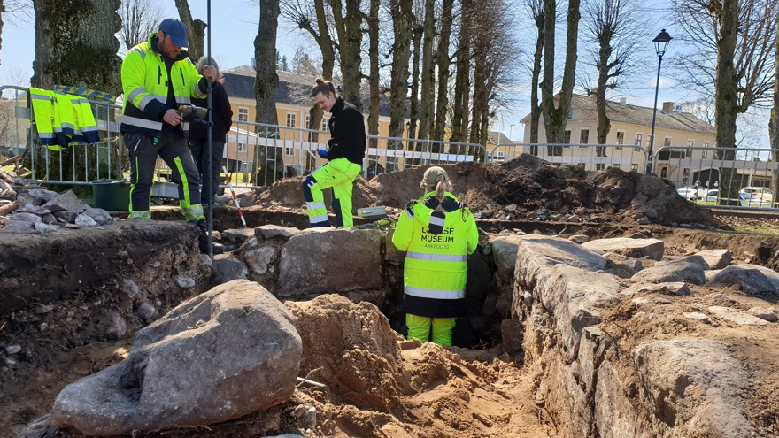 Flera arkeologer står vid en utgrävning av stenfundamentet till en byggnad