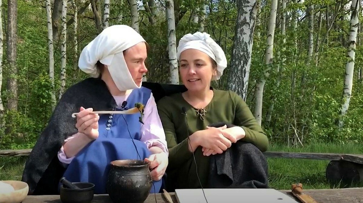 Två kvinnor i medeltida kläder äter soppa