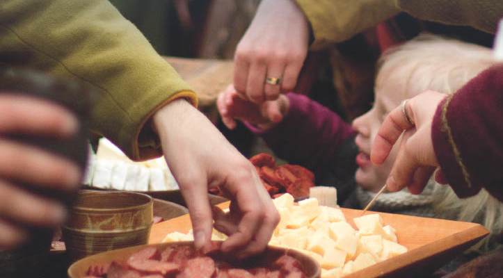 En närbild på ett barn och händer som plockar bland skålar med mat