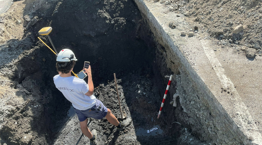 An archaeologist standing in a hole in the ground with measuring instruments.
