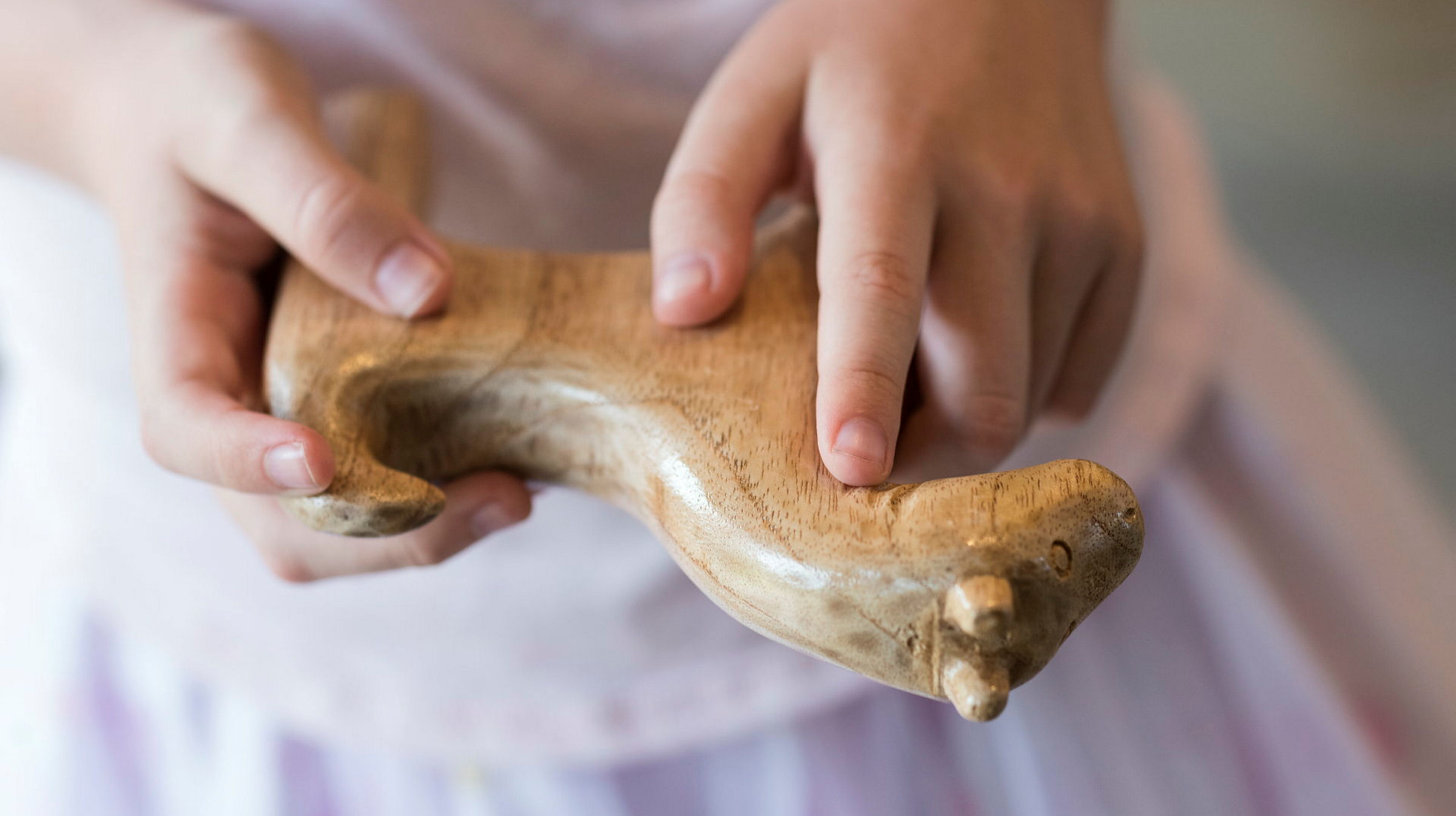 Ett par barnhänder håller i och känner med fingrarna över en trähäst.