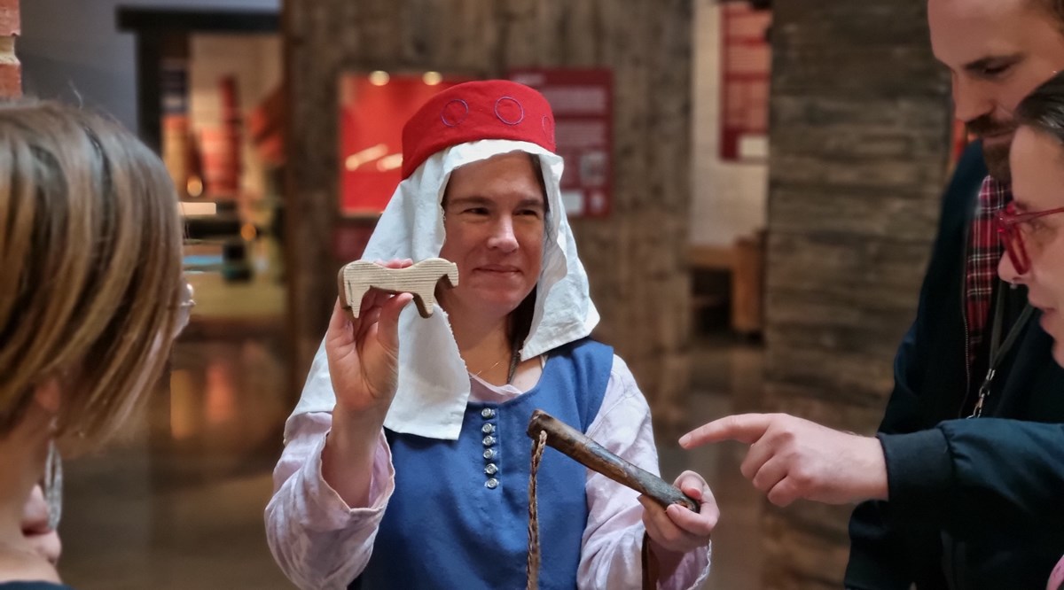 En kvinna i medeltidskläder håller upp historiska föremål