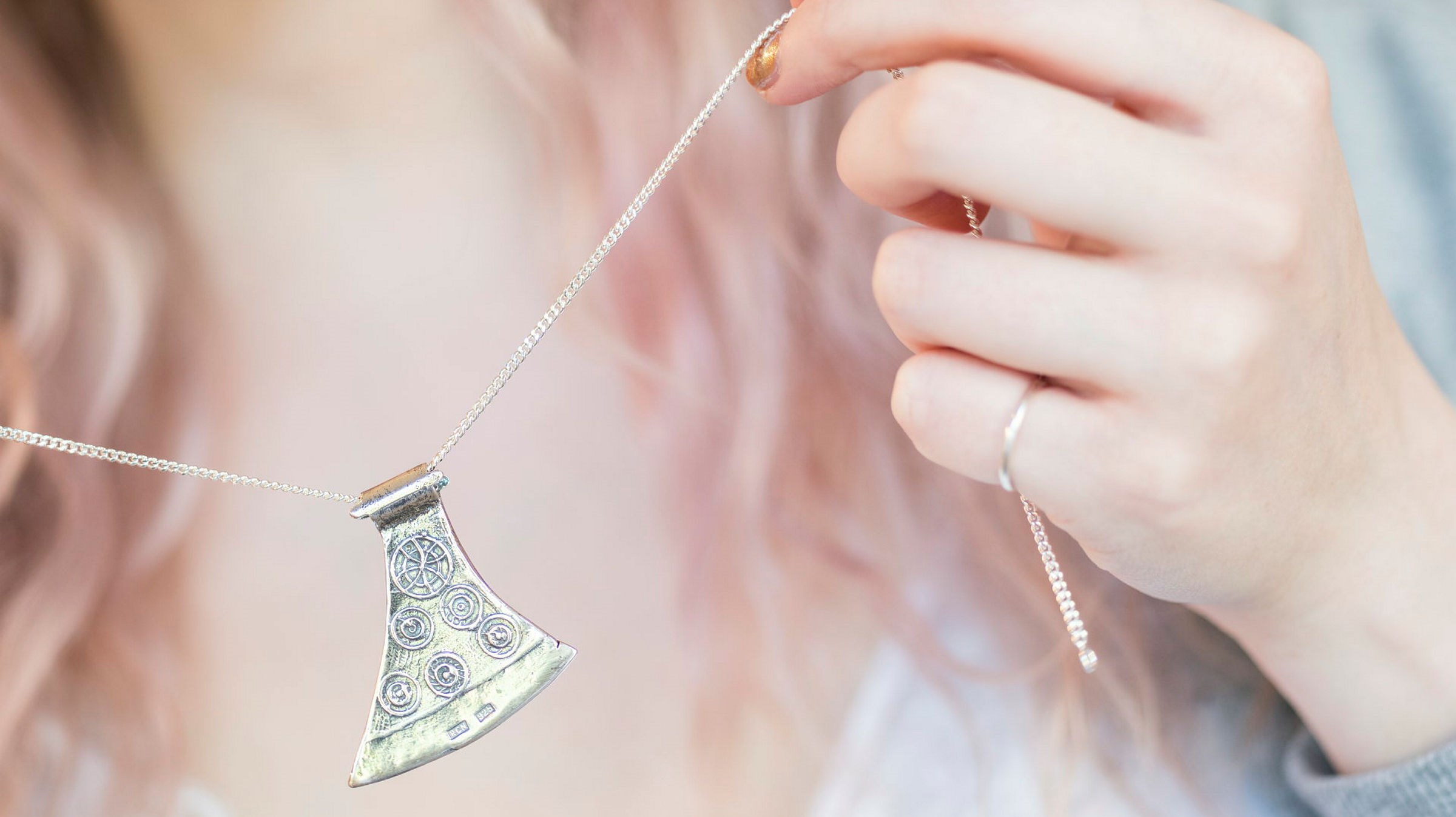En hand håller i ett halsband med en silveryxa på