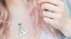 En hand håller i ett halsband med en silveryxa på