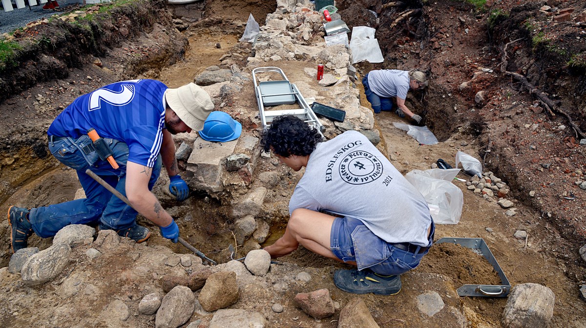 Tre arkeologer gräver ut en stenmur