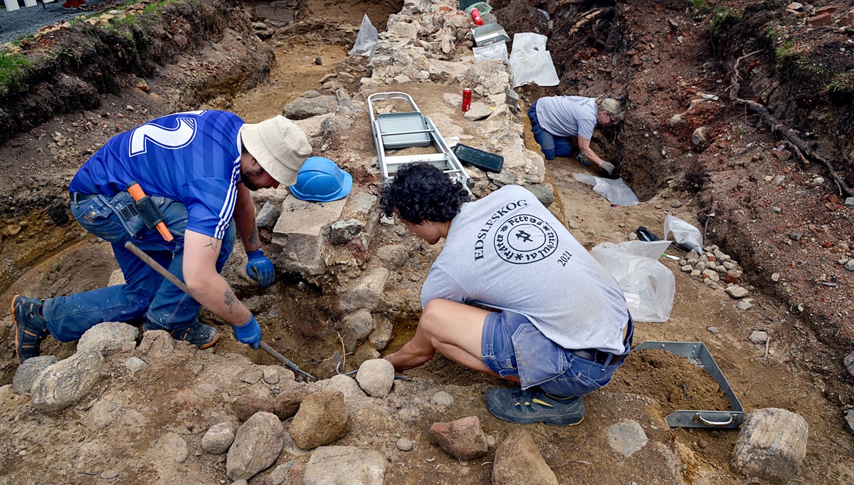 tre arkeologer gräver ut en stenmur