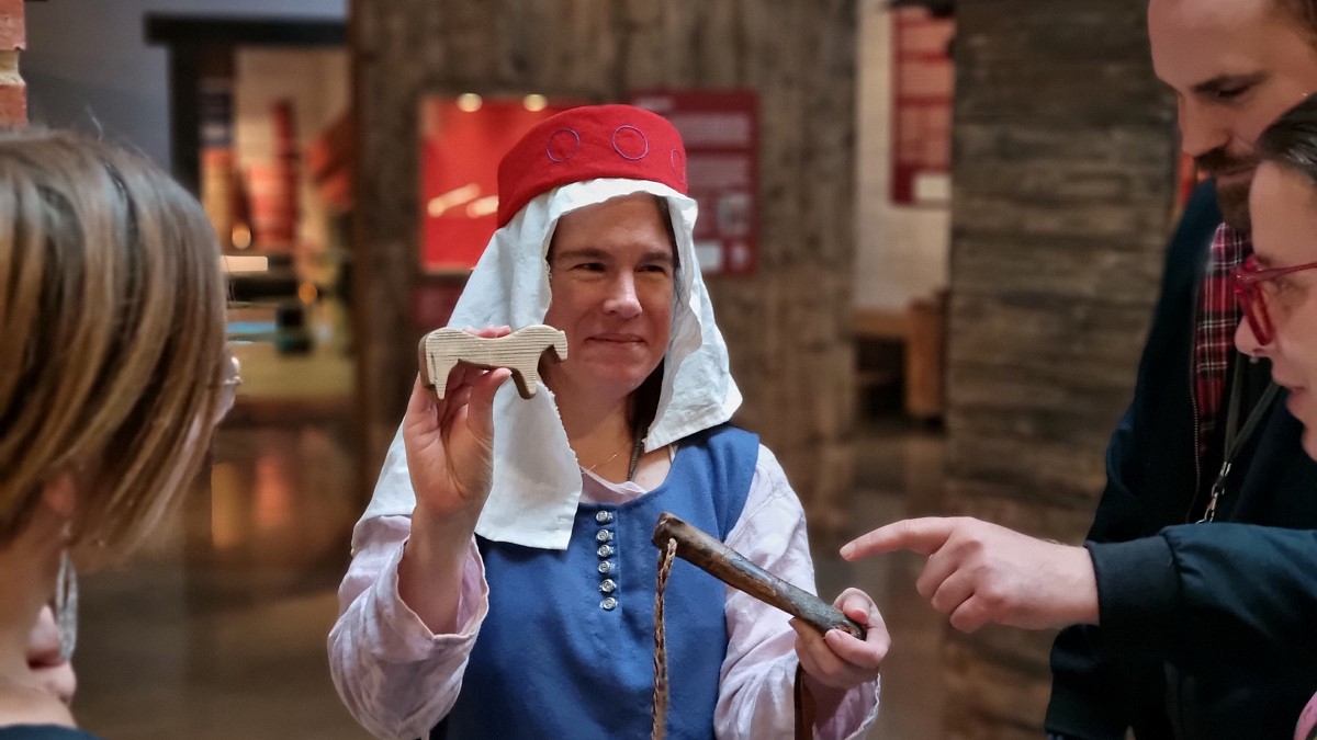 En kvinna iklädd medeltida kläder visar upp en trähäst.