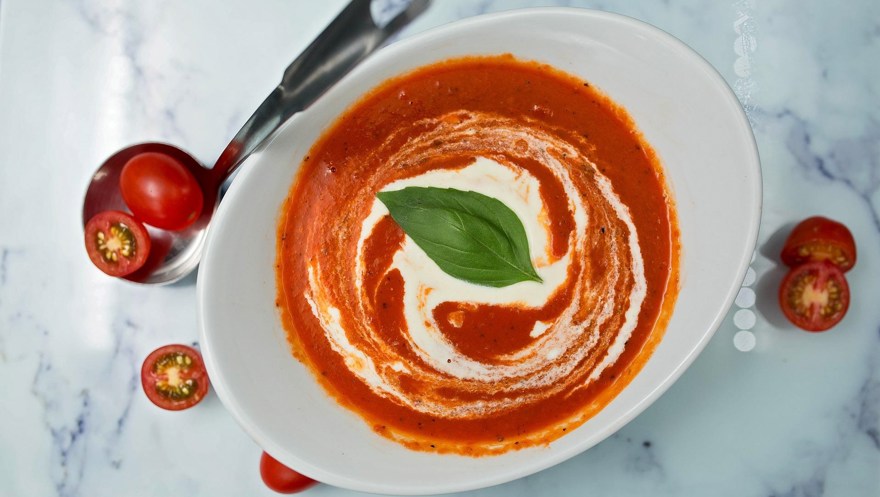 en skål tomatsoppa står på en marmorbänk
